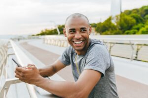 Man smiling outside and looking sideways while texting on his phone